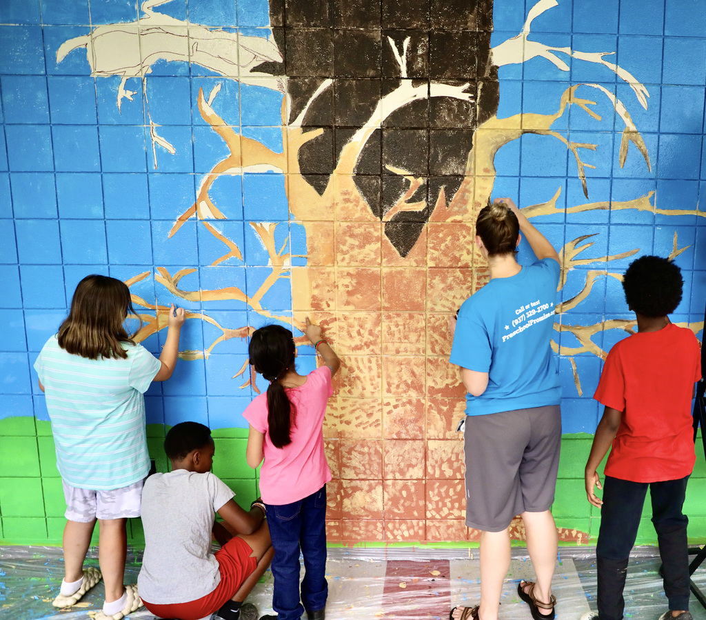 A group picture of Principal Warner working with her students on the new tree mural in the school's main hallway